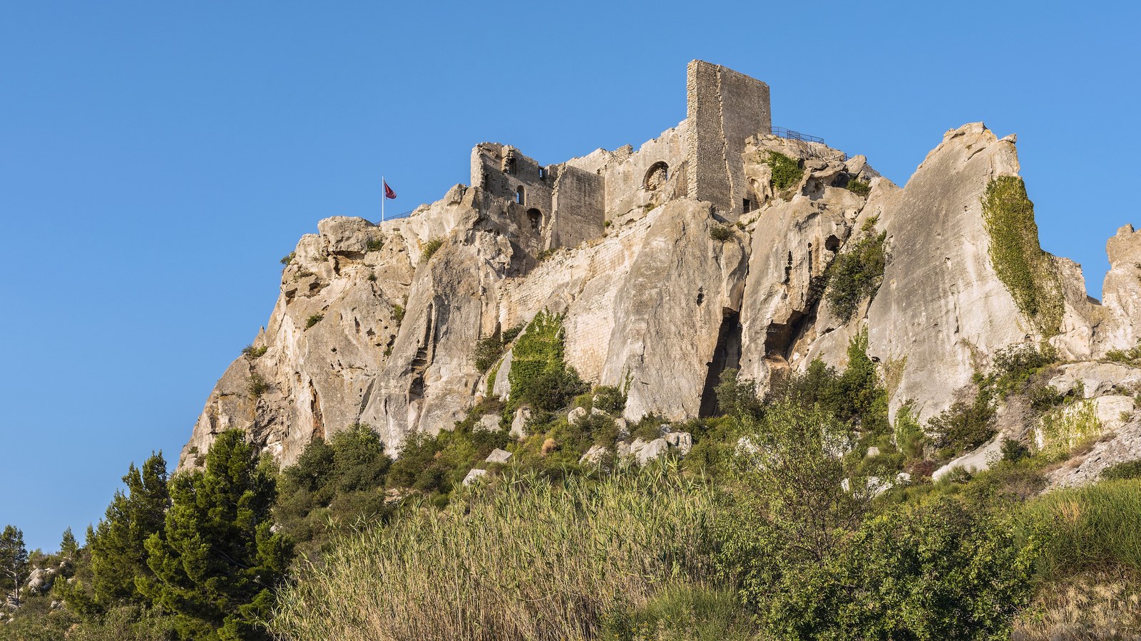 Les ruines du château des Baux-de-Provence, donjon carré et murailles taillées dans un éperon de calcaire blanc, sous un ciel bleu
