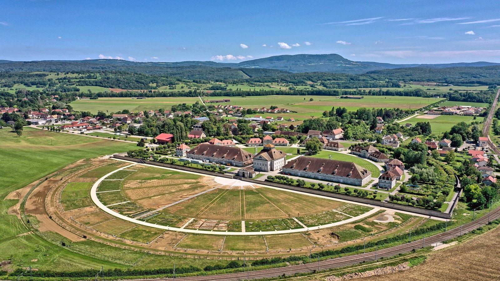 Vue aérienne de la saline royale d'Arc-et-Senans en demi-cercle, avec le cercle de jardins en cours d'aménagement au premier plan