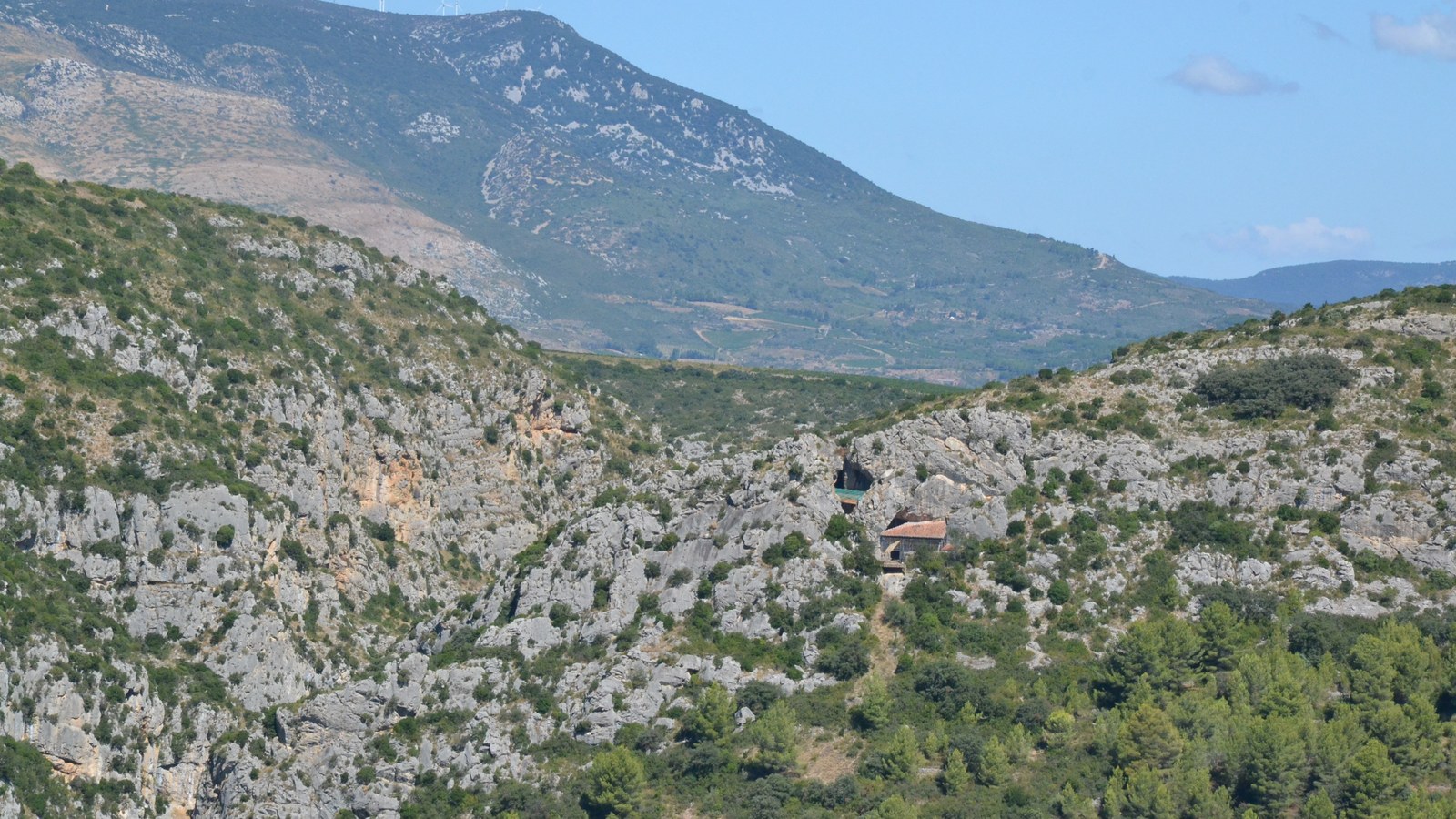 L'entrée de la Caune de l'Arago dans une falaise calcaire des gorges du Verdouble, avec la montagne de Tauch en arrière-plan