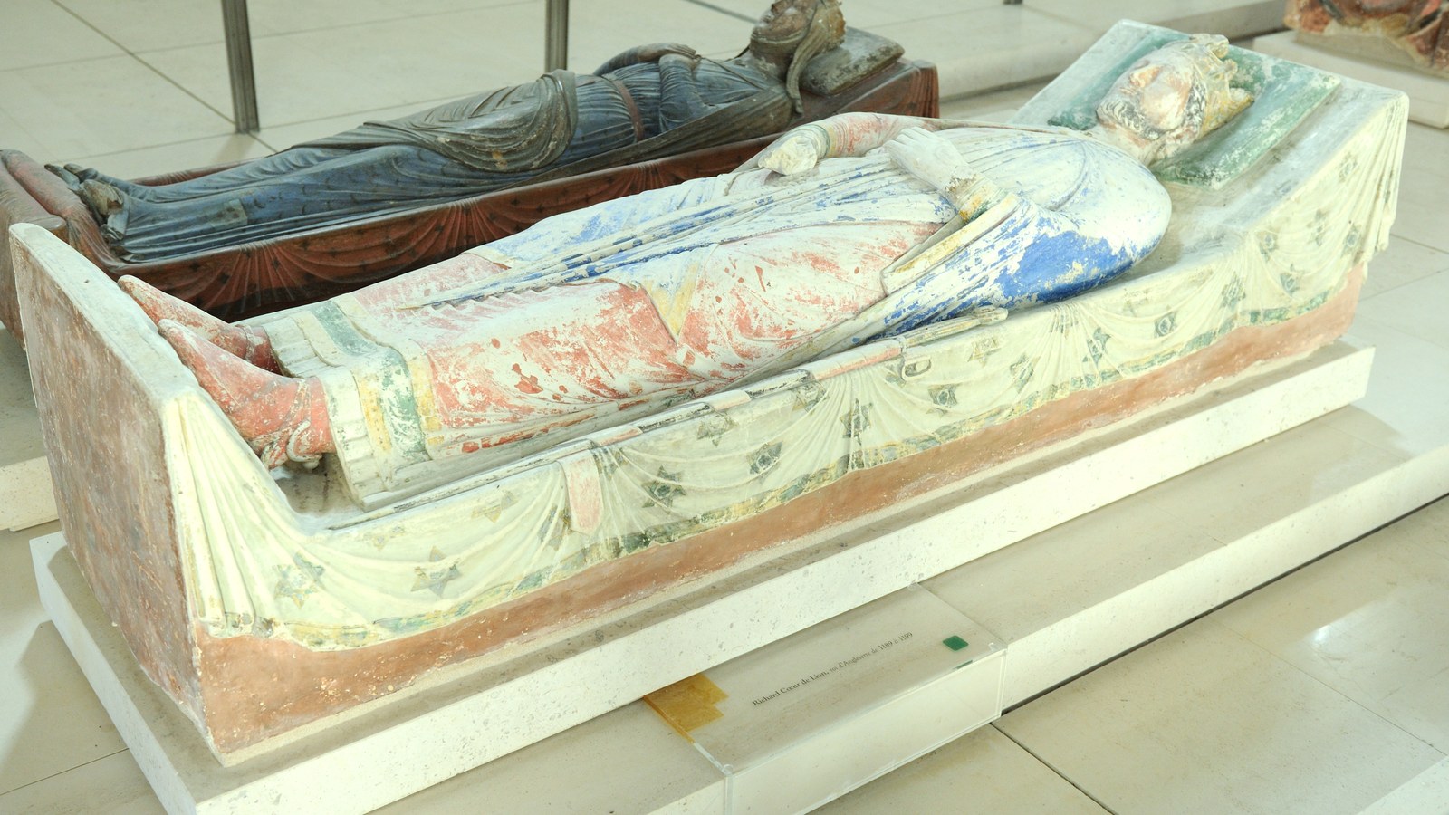 Gisant polychrome de Richard Cœur de Lion dans l'abbatiale de Fontevraud, couronné et vêtu d'un manteau peint, avec un autre gisant en bois sombre à l'arrière-plan