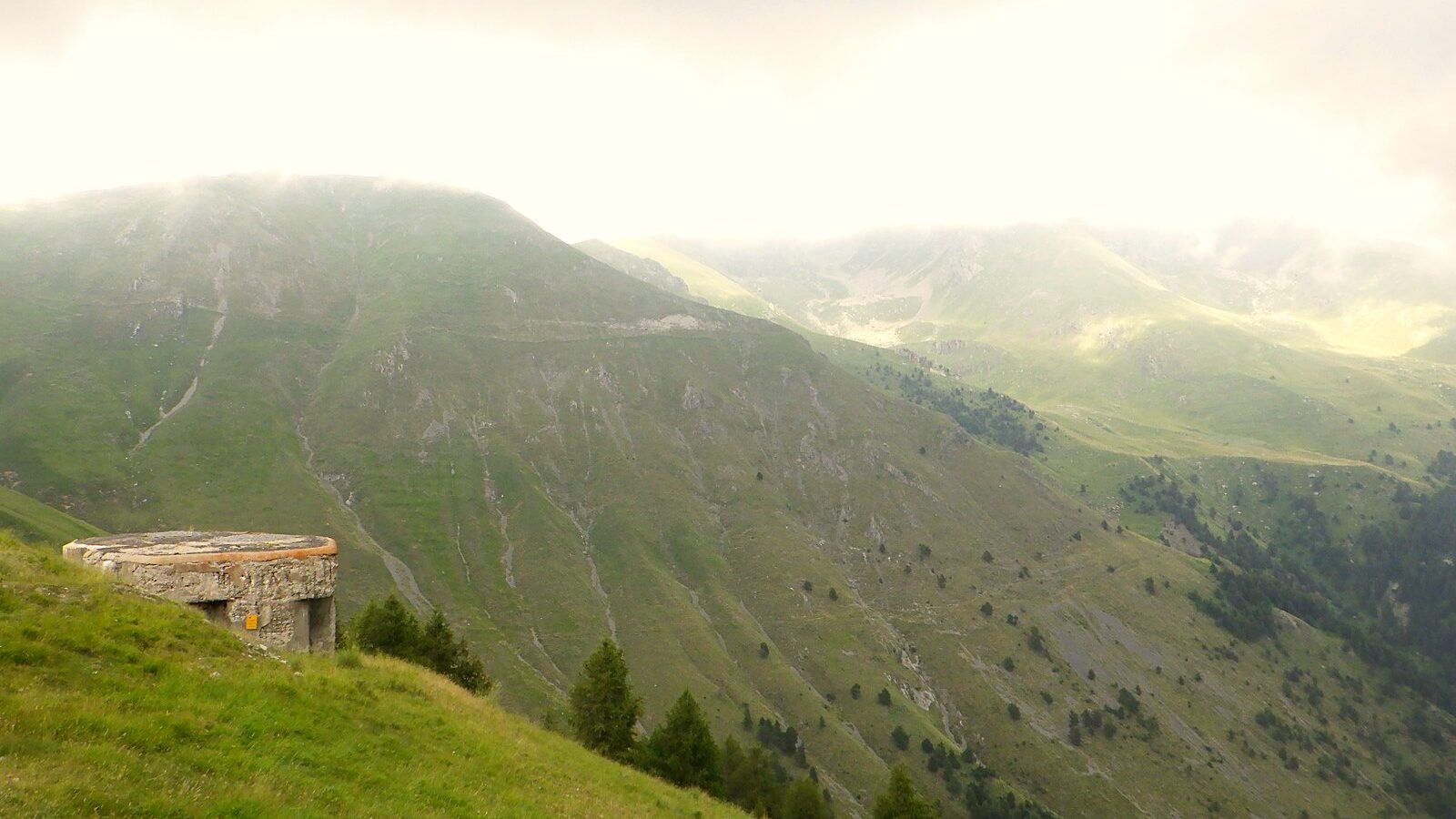 Un petit ouvrage bétonné sur un versant d'alpage, face aux crêtes des Alpes-Maritimes