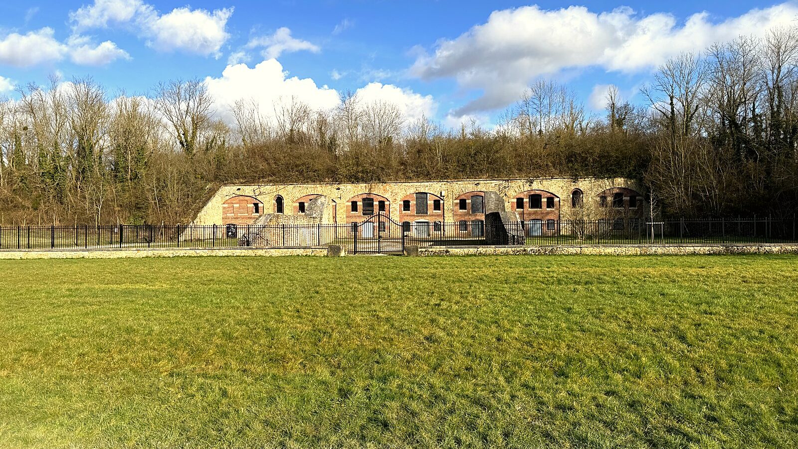 La façade voûtée du fort de Chelles derrière son glacis herbeux, en Seine-et-Marne