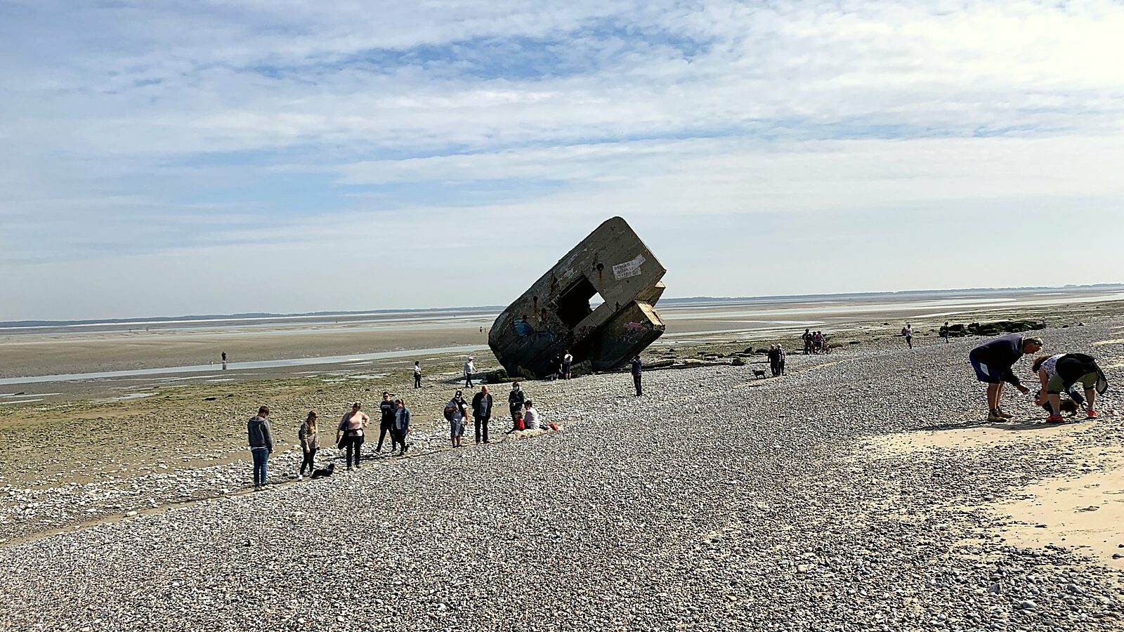 Un blockhaus basculé sur le cordon de galets du Hourdel, couché sur le flanc, avec des promeneurs autour