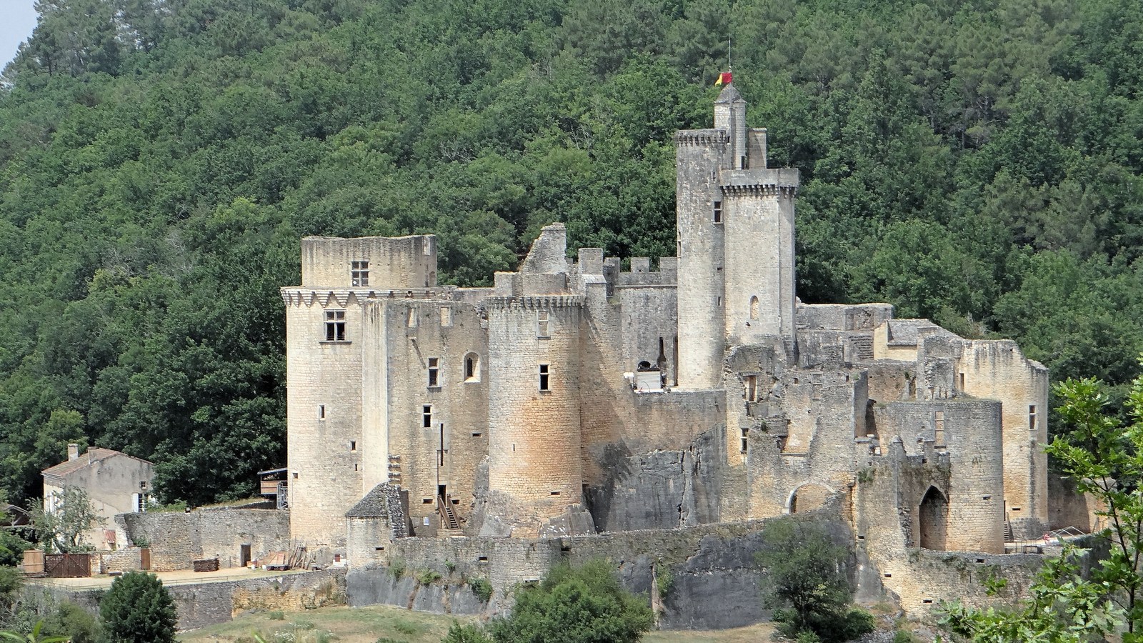 Le château de Bonaguil et ses tours sur leur éperon rocheux, devant une colline boisée