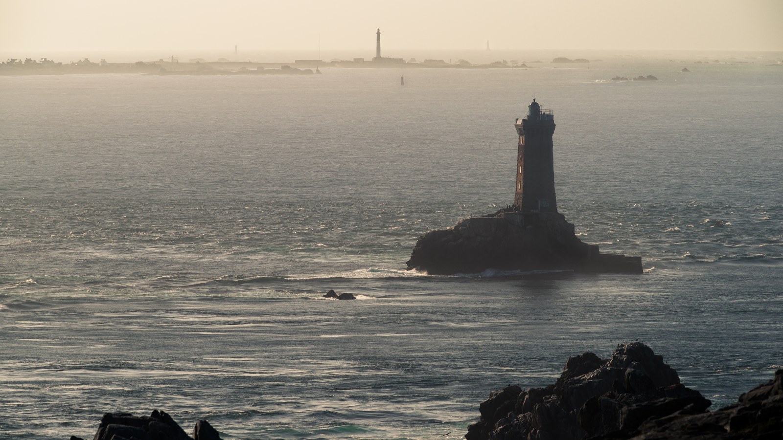 Le phare de la Vieille au premier plan, avec l'île de Sein basse et plate à l'horizon, vus depuis la pointe du Raz