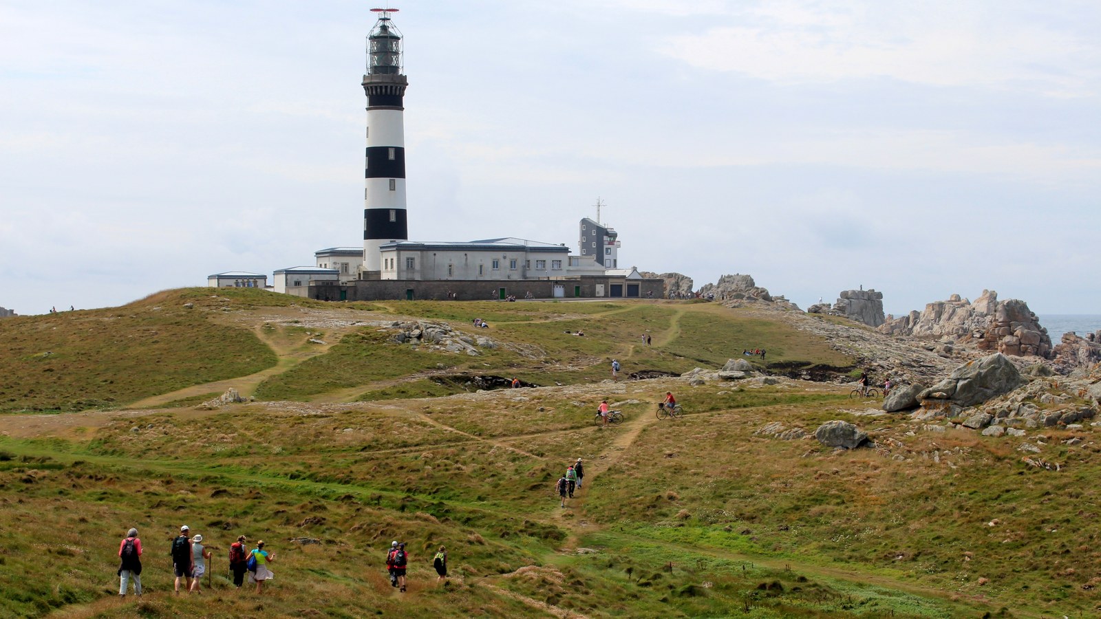 Le phare du Créac'h à bandes noires et blanches et ses bâtiments, au-dessus de la lande d'Ouessant parcourue par des randonneurs