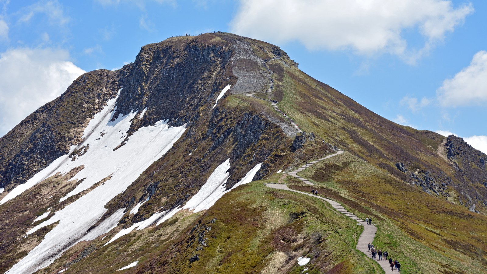 Le puy Mary et le sentier qui mène à son sommet, avec des névés sur le versant et des randonneurs