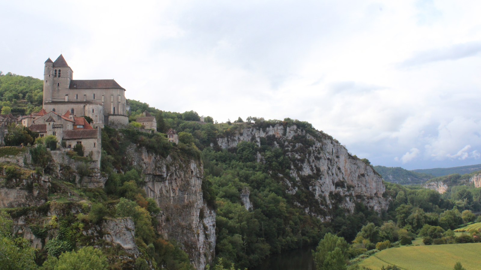 Le village de Saint-Cirq-Lapopie et son église au bord d'une falaise calcaire dominant la vallée boisée du Lot