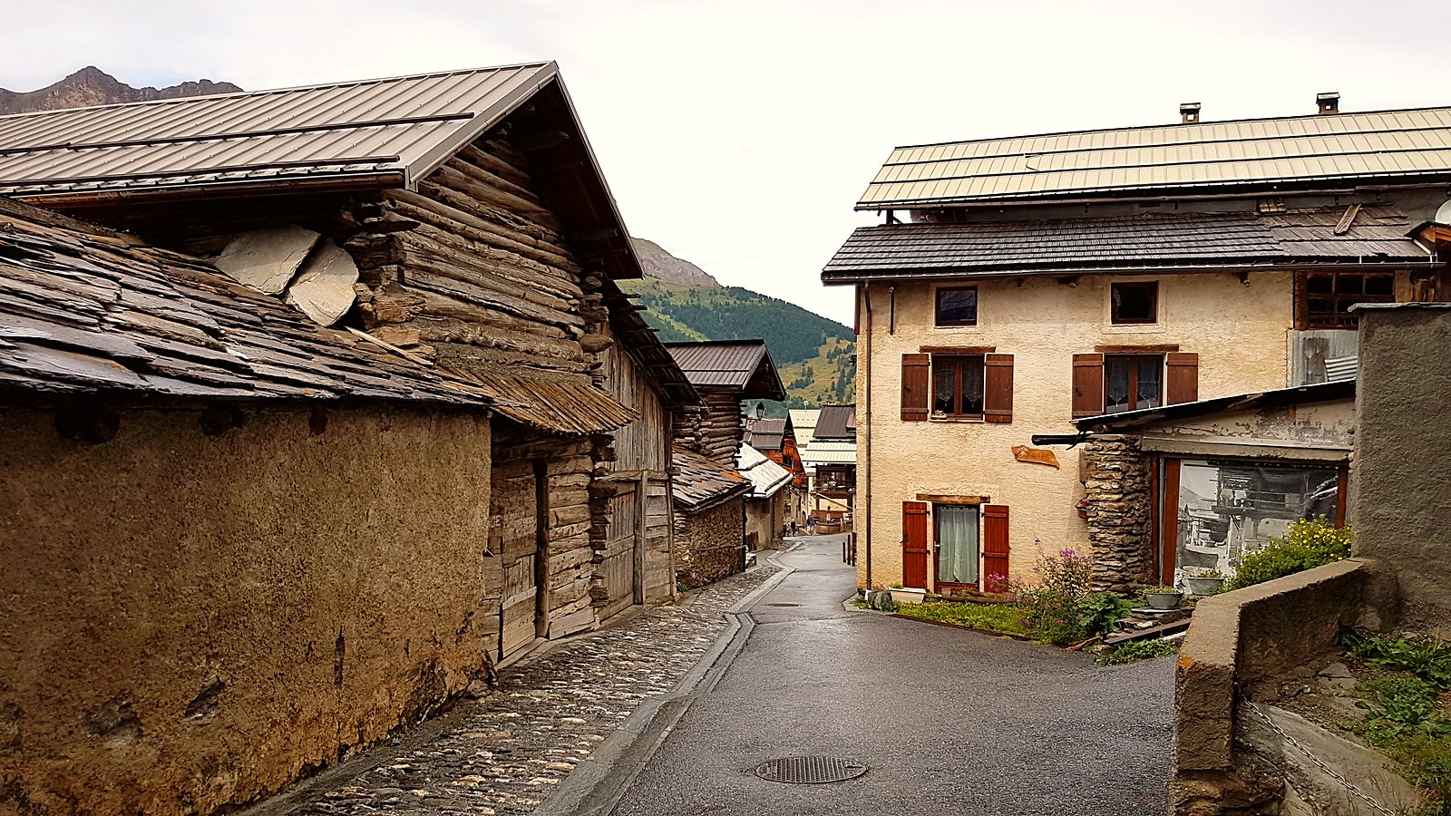 Une rue de Saint-Véran, avec une maison à rez-de-chaussée de pierre et fuste de troncs empilés