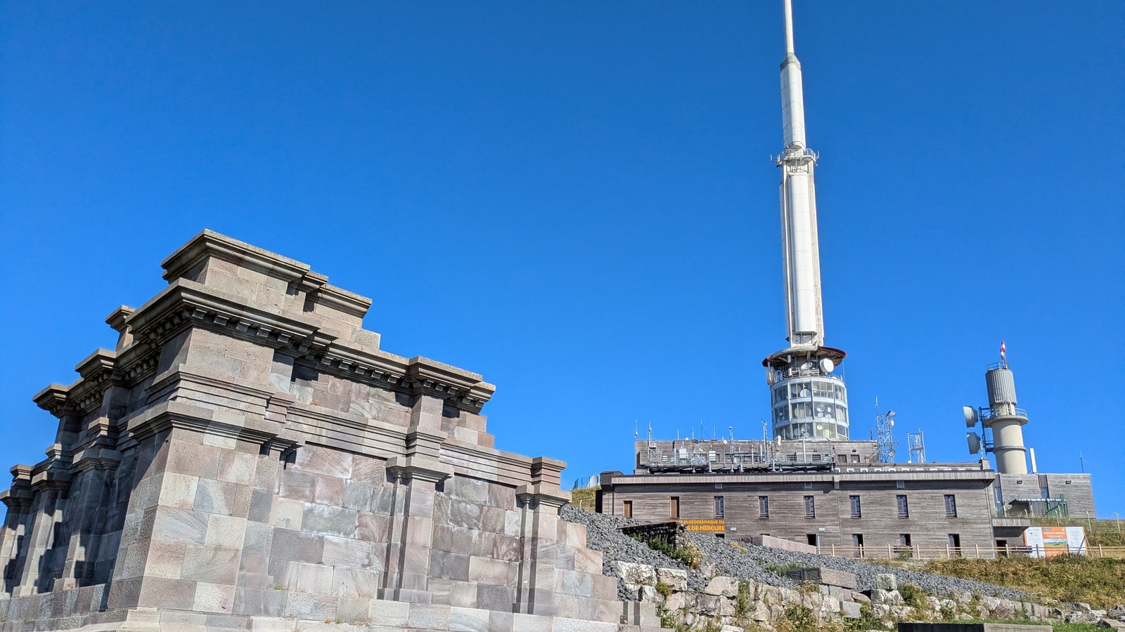 Un angle reconstruit du sanctuaire de Mercure en blocs de trachyte, au sommet du puy de Dôme, devant l'ancien chalet de l'observatoire et l'antenne de télédiffusion