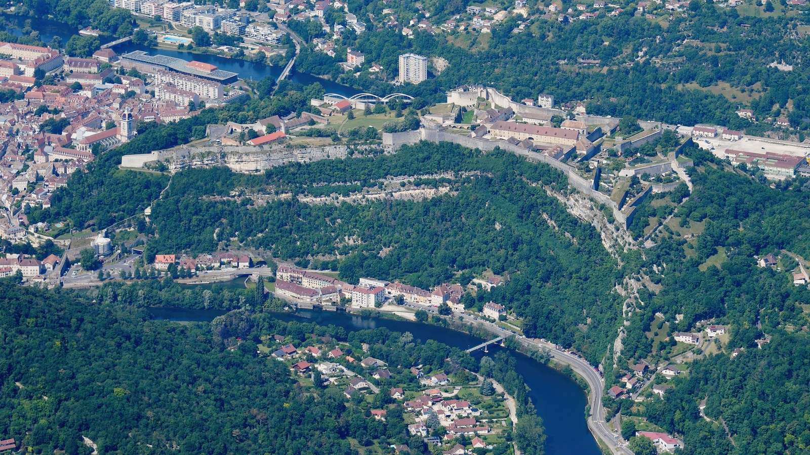 Vue aérienne de la citadelle de Besançon sur son éperon boisé, avec le Doubs au premier plan et la vieille ville à gauche