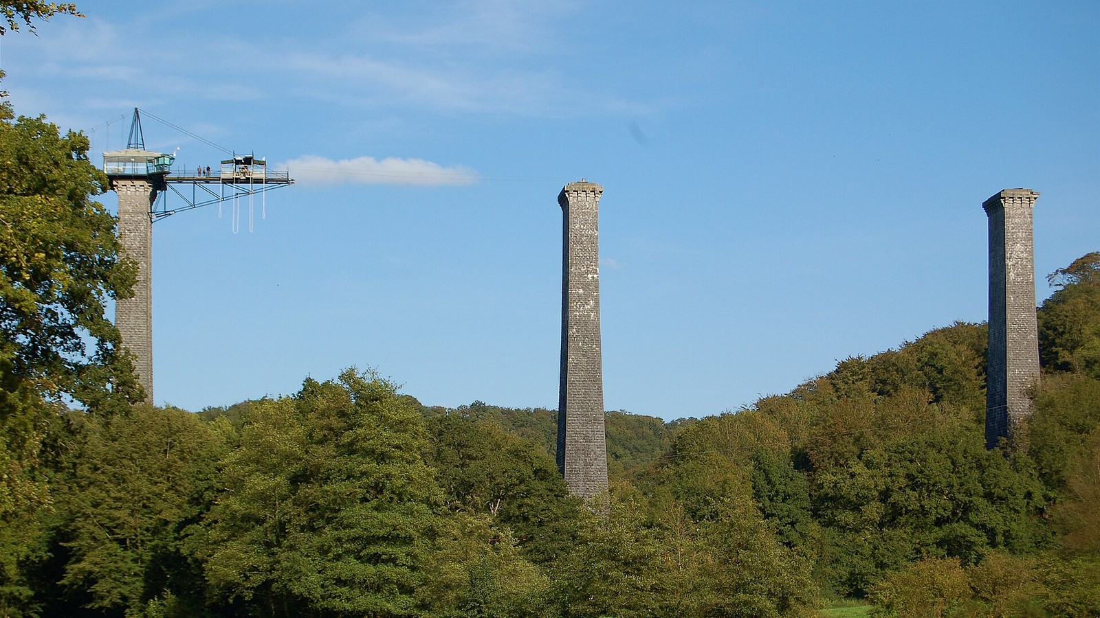 Trois piles de pierre de l'ancien viaduc de la Souleuvre au-dessus des arbres, la première portant la plateforme de saut à l'élastique