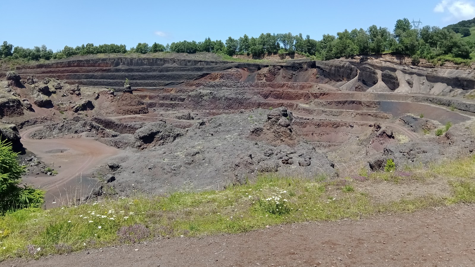 Ancienne carrière du puy de Lemptégy taillée en paliers de scories rouges et noires, sous un ciel bleu